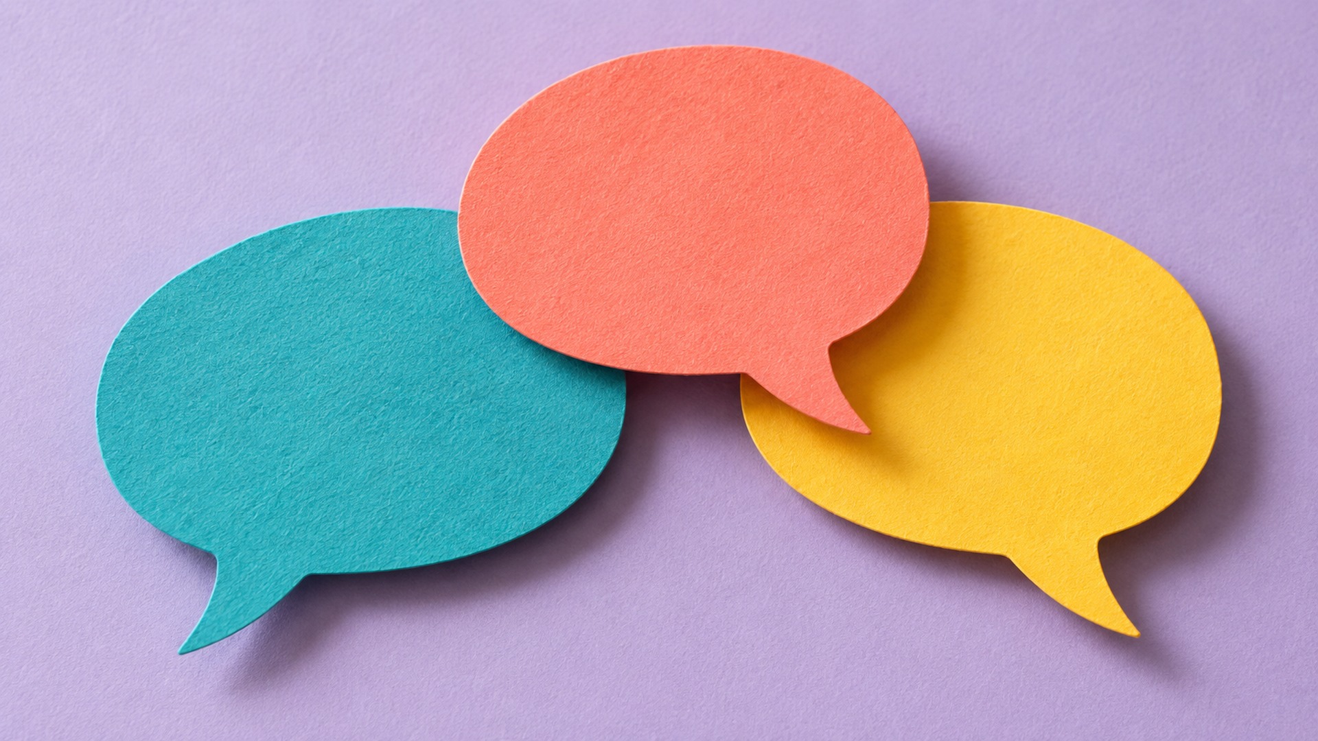Coral, turquoise and yellow paper speech bubbles on a lavender surface.