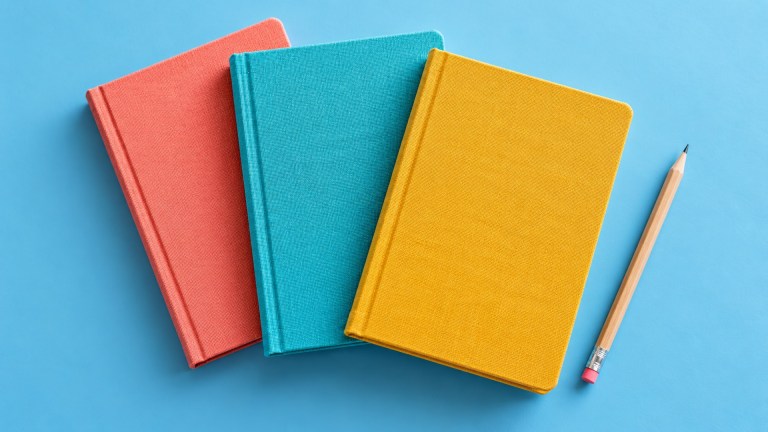 Coral, turquoise and yellow notebooks arranged on a blue surface beside a pencil.
